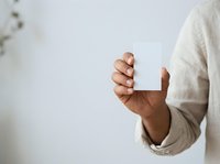 Adult male with medium brown skin tone holding blank white card in hands, wearing casual beige sweater, ideal for business cards, invitations, and promotional designs.