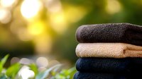 Folded clean bath towels stacked in soft natural sunlight with blurred green garden background and bokeh effect, fresh laundry concept for spa and wellness.