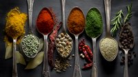 Aromatic colorful spices and herbs in vintage silver spoons on dark background, arranged in row for cooking and seasoning food.