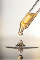 Golden liquid drop falling from dropper with mirror reflection on light surface, capturing moment before impact in macro photography. Suitable for cosmetic advertising.