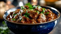 Tender beef chunks in rich brown gravy garnished with fresh herbs, served in blue ceramic bowl. Traditional homestyle meat stew with aromatic sauce and parsley.