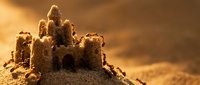 Sandcastle on beach at sunset with golden warm light creating magical atmosphere for summer vacation and childhood memories.