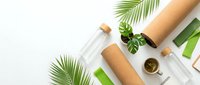 Flat lay composition featuring eco-friendly cosmetic packaging with cork and glass bottles, green plant leaves, and natural skincare products on white background for sustainable beauty branding.