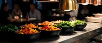 Young chef preparing colorful vegetables in professional kitchen with heat lamp, showcasing culinary preparation and food service for restaurant, catering, cooking content.
