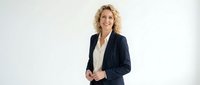 Professional blonde businesswoman in navy blazer smiling confidently against white background, corporate headshot for marketing materials.