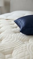 Navy blue pillow resting on quilted cream bedding with white pillows in soft bedroom setting. Ideal for home decor, interior design, and lifestyle content.