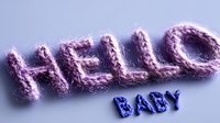 Knitted purple hello text with blue baby word below on light background, cozy handmade letters for nursery decor and baby shower announcements.