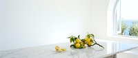Fresh lemons spilled on white marble countertop near bright window, ideal for food styling, culinary blogs, healthy eating content, and kitchen design projects.