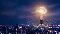 Glowing light bulb with brain inside floating over night city skyline with digital network connections representing innovation and creative thinking.