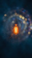 Glowing vintage filament bulb with warm orange light against dark blue bokeh background, sparks flying, suitable for innovation, energy, and creativity concepts.