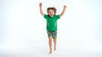 Happy young boy jumping with arms raised wearing green shirt and shorts on white background isolated for design use.