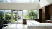 Modern minimalist kitchen with marble island and floor-to-ceiling windows overlooking lush garden. Open plan design with natural light and contemporary finishes.