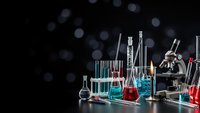 Laboratory glassware with colorful chemical solutions and microscope on dark background with bokeh lights for scientific research and education.