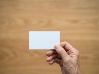 Senior adult hand holding blank white business card against wooden background, suitable for mockups, branding presentations, and corporate identity designs.