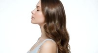 Young woman with long wavy brown hair in profile showing healthy shiny locks against white background for beauty and haircare advertising campaigns.