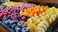 Fresh colorful fruit platter with frozen berries, mango, pineapple and citrus slices arranged in rows, creating vibrant pattern for healthy eating and food service.