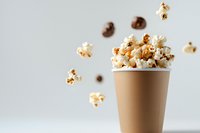 Fresh popcorn flying out of brown paper cup on light background, dynamic food photography with levitating kernels for cinema and snack concepts.