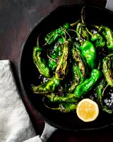 Grilled green padron peppers with sea salt and lemon in cast iron pan on dark background. Traditional Spanish tapas dish for restaurant menu.