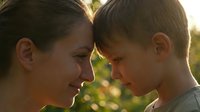 Young Caucasian mother and son sharing tender moment outdoors with warm golden sunlight creating intimate family bonding scene in natural setting.