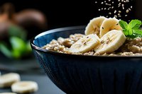 Healthy breakfast bowl with oatmeal, fresh banana slices and mint garnish on dark background for nutritious morning meal concepts.