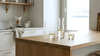 Modern kitchen island with white marble countertop and wooden base, featuring minimalist decor, glass vases, and natural light from window for contemporary home design projects.