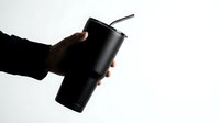 Hand holding a black insulated tumbler with a metal straw on a light background, showcasing modern reusable drinkware for eco-friendly lifestyle.