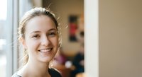 Young Caucasian woman with blonde hair smiling warmly at camera in bright indoor setting with natural window light for lifestyle and portrait projects.