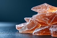 Amber gummy candies dusted with sugar crystals on dark blue surface, ideal for confectionery, food photography, and candy packaging design projects.