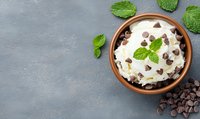Creamy dessert with chocolate chips and fresh mint leaves in ceramic bowl on grey concrete background, top view with copy space for menu or recipe.