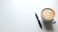 Coffee cup with latte art and pen on white desk surface for business workspace and morning routine concepts.