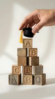 Hand placing miniature graduation cap on wooden alphabet blocks pyramid representing educational achievement and academic success concept.
