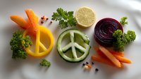 Peace symbols made from fresh vegetables and citrus fruits on white background. Creative healthy food art composition with cucumber, orange, beet and carrot slices.