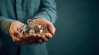 Businessman hands protecting miniature house model with keys symbolizing real estate investment security and property insurance coverage concept.