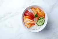 Fresh salmon and tuna sashimi bowl with sliced cucumber and steamed rice on marble background, garnished with sesame seeds and herbs for Asian cuisine.