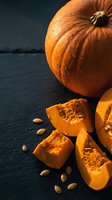 Fresh orange pumpkin cut into slices with seeds on dark slate background for autumn cooking and seasonal recipes.