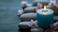 Zen spa composition with burning blue candle, smooth stones and delicate pink cherry blossoms on dark wooden surface for relaxation and meditation.