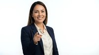 Professional Hispanic businesswoman in navy suit pointing at camera with confident smile on white background for corporate presentations.