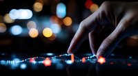 Professional DJ mixing music on digital controller with colorful bokeh lights in nightclub background, close up view of hands adjusting controls.