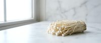 Bunch of white enoki mushrooms on marble surface with natural window light, suitable for food photography, culinary content, and restaurant menus.