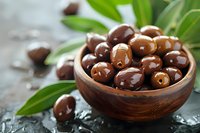 Fresh dark chocolate covered almonds in wooden bowl with green leaves on dark stone background, selective focus. Healthy snack concept.