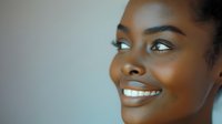Close-up portrait of young African woman with radiant smile and glowing skin against soft neutral background, conveying happiness and confidence.