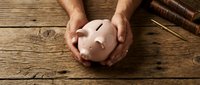 Mature male hands holding a pink piggy bank on a rustic wooden table, symbolizing savings, financial security, and retirement planning.