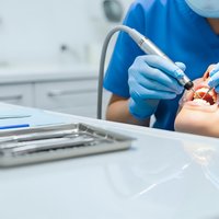 Dentist performing dental procedure on patient in modern clinic with professional equipment and sterile environment for oral healthcare treatment.