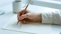 Person writing on paper with brush pen at desk with coffee mug, workspace organization and creative work concept for design projects.