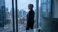 Senior businesswoman in dark blazer standing by floor-to-ceiling windows overlooking urban cityscape, contemplating skyline from high-rise office building for corporate leadership and professional success concepts.