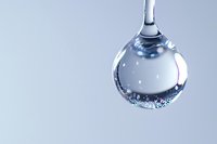Clear water droplet with tiny air bubbles suspended inside, hanging from thin stream against light blue background.