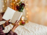 Woman with henna-decorated hands reading open book during festive holiday season with warm bokeh lights and decorated background.