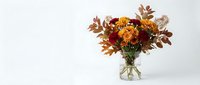 Autumn flower arrangement with orange chrysanthemums and colorful fall foliage in glass vase on white background for seasonal home decor and thanksgiving designs.