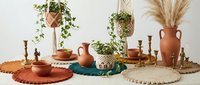 Bohemian home decor arrangement with terracotta pottery, woven placemats, dried pampas grass and hanging plants creating warm earthy interior styling.