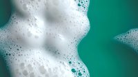 Foamy white soap bubbles and suds on vibrant teal green background for cleaning products advertising and hygiene campaigns.